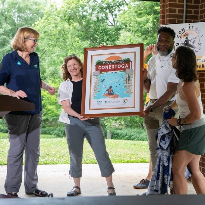 The PA DCNR Secretary, Cindy Dunn and four other individuals unveiling the poster for the 2026 River of the Year. 