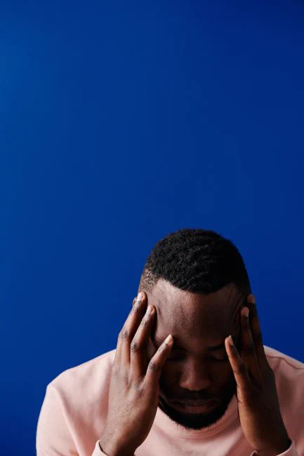 A young African American man with hands on his head against a blue background, expressing stress.