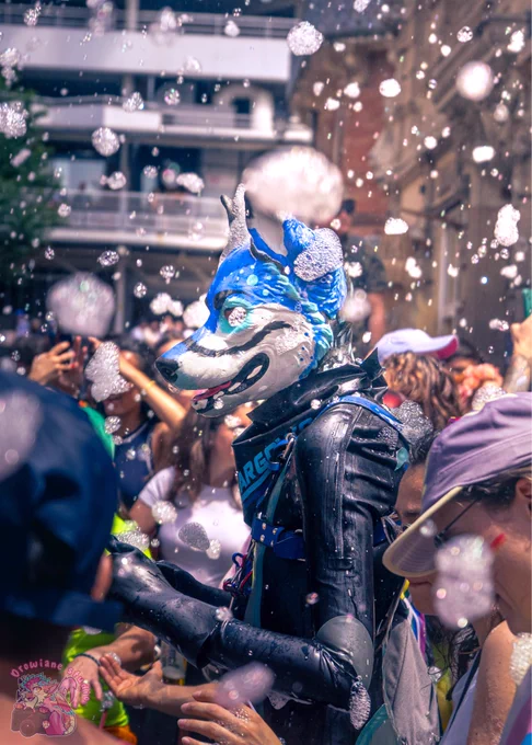 a blue grey and black shiny dog dancing in the crowd at a gay pride. He is surrounded by flying foam