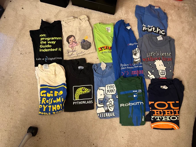 A collection of vintage computer programming T-shirts is displayed folded on the floor.