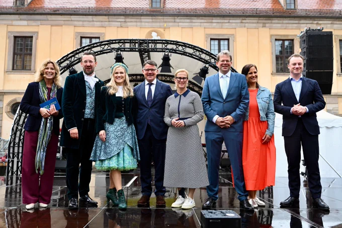Eine Gruppe von sieben Personen posiert für ein Foto auf einem Platz vor einem Gebäude.