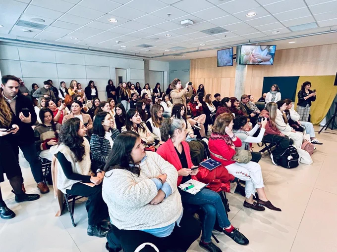 Público asistente al conversatorio, compuesto por decenas de personas sentadas y de pie, siguiendo las intervenciones. Algunas toman fotografías o registran la actividad con sus teléfonos móviles.