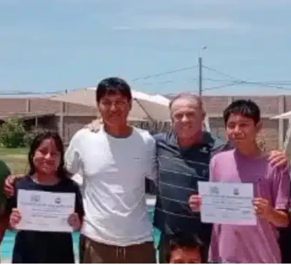 four people are standing next to each other, one dark haired man in a white shirt in the middle. He's Pablo, former fisherman, now SwimTayka swimming instructor. Around him, children are holding up what looks like certificates, probably following their swimming lessons with Pablo. They all have their arms around each other's shoulders