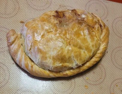 Photo of a beautifully browned pastry hand pie on a tan silicone baking liner with many concentric circles printed on it.