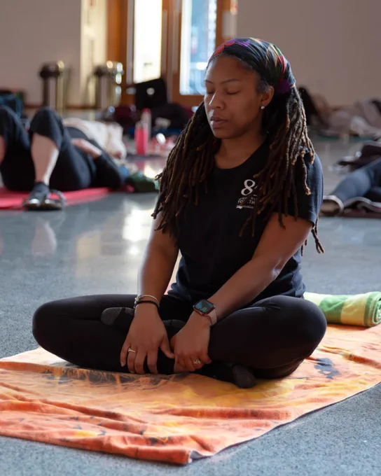 Person sitting cross-legged on an orange towel with their eyes closed in meditation