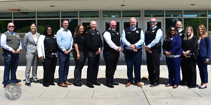 A group of individuals stands in front of a BOP facility, many wearing vests with badges. 