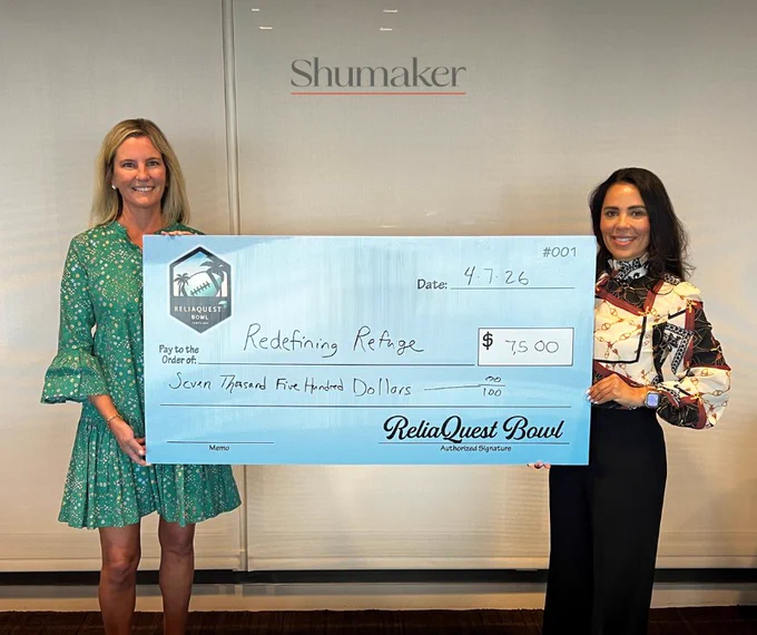 Two women hold a large check made out to Redefining Refuge for $7,500. The event appears professional and celebratory.