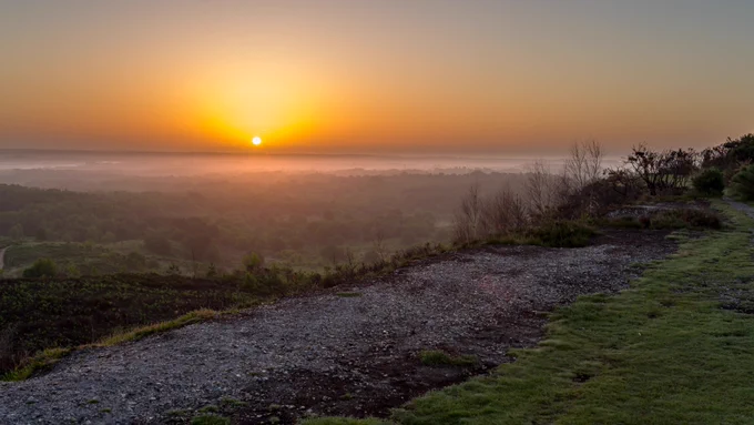 Landscape photograph of sunrise from Caesar's Camp Hill Fort, Farnham, Surrey, UK, 11 June 2022.