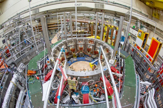 Overhead view of the NSTX-U, which has a large number of complex electronics and support beams. There is a circular opening in the middle where the magnets at the center of the device will be placed.