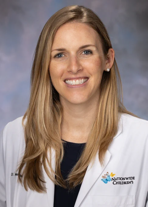 Woman doctor wearing a lab coat smiling with long blonde hair.
