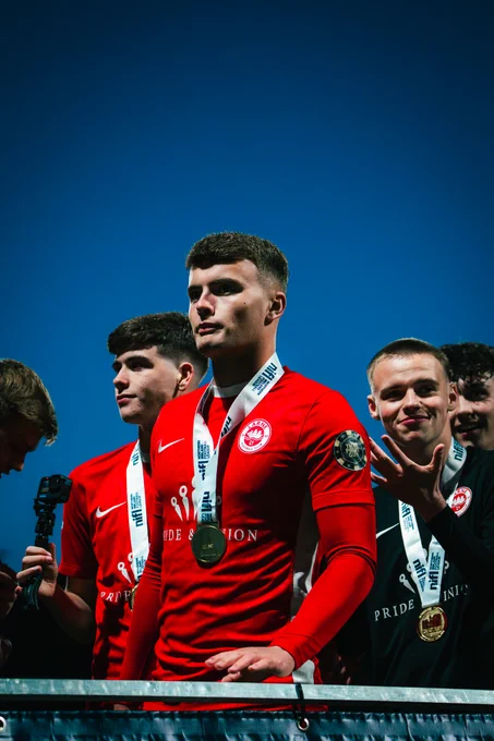A group of young football players in red jerseys celebrate their success, wearing medals under a clear blue sky.