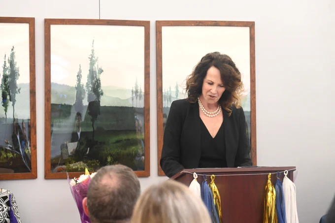 A woman speaks at a podium during a Community Justice Support Center ceremony as attendees listen from the audience.