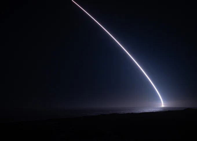 Bright curved light trail streaks across a dark night sky above a silhouetted horizon.