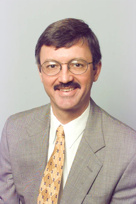 Thomas Anthony, M.D. sitting for a portrait photo. He is wearing a tan suit and yellow diamond patterned tie.