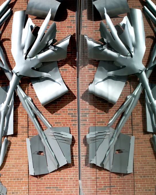 An abstract metal sculpture on a brick wall reflected from inside to outside.