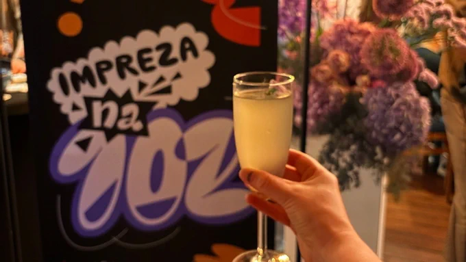 A hand holds up a flute glass in front of a sign for the Woo Community Event at WCEU 2026.