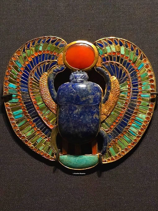 This Jewelry Was Meant to Bring a Pharaoh Back to Life…

Hidden deep inside the tomb of Tutankhamun in the mysterious Valley of the Kings, archaeologists uncovered something that feels almost… alive.

At first glance, it looks like a beautiful piece of jewelry. But look closer—and it tells a story that refuses to die.

At its center lies a deep blue scarab, carved from precious stone, its wings spread wide as if ready to rise. This is not just decoration. To the ancient Egyptians, the scarab represented Khepri—the god who pushed the sun across the sky each day, symbolizing rebirth, resurrection, and the promise that death is never the end.

Above it, a glowing red sun disk seems to hover, held carefully in place. Around it, vibrant colors—turquoise, gold, and glass—still shine as if they were crafted yesterday… not over 3,300 years ago.

But here’s where it gets unsettling.

This ornament was not made to be admired. It was made for the afterlife.