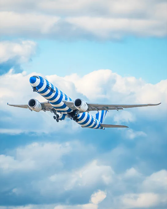 Airplane with blue and white stripes flying upward against a cloudy sky.
