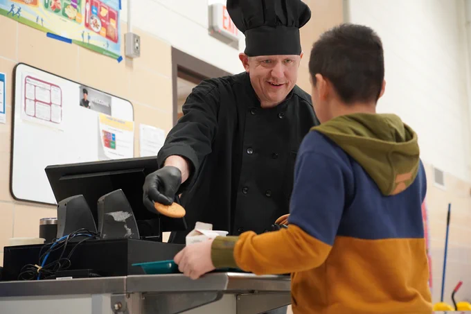 Food Services staff smiling and giving a cookie to a student