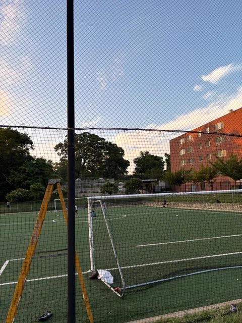 Empty outdoor tennis court with a net and a wooden ladder beside it during early evening under a partly cloudy sky.