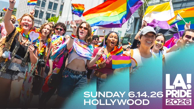 Crowd of smiling Pride attendees marching through a city street, waving rainbow and LGBTQ  community flags. People of diverse backgrounds cheer and celebrate in bright sunlight, with large Pride flags visible above the crowd. Promotional text reads: “Sunday 6.14.26 Hollywood” and “LA! Pride 2026.”