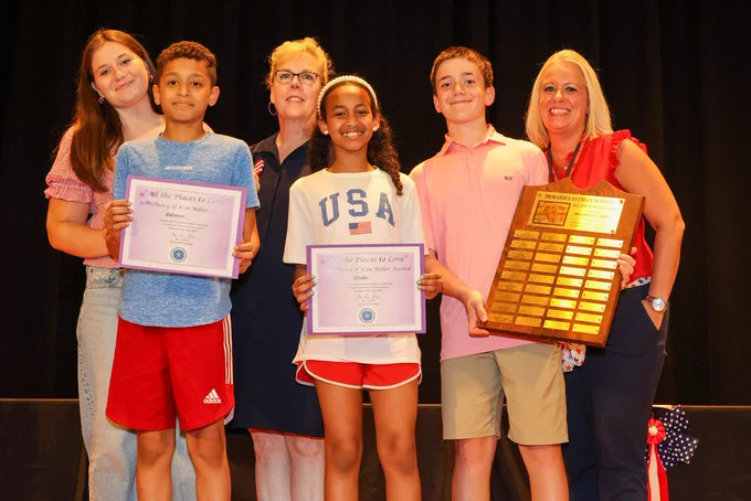 Students hold up award cerficates on stage with presenters and staff