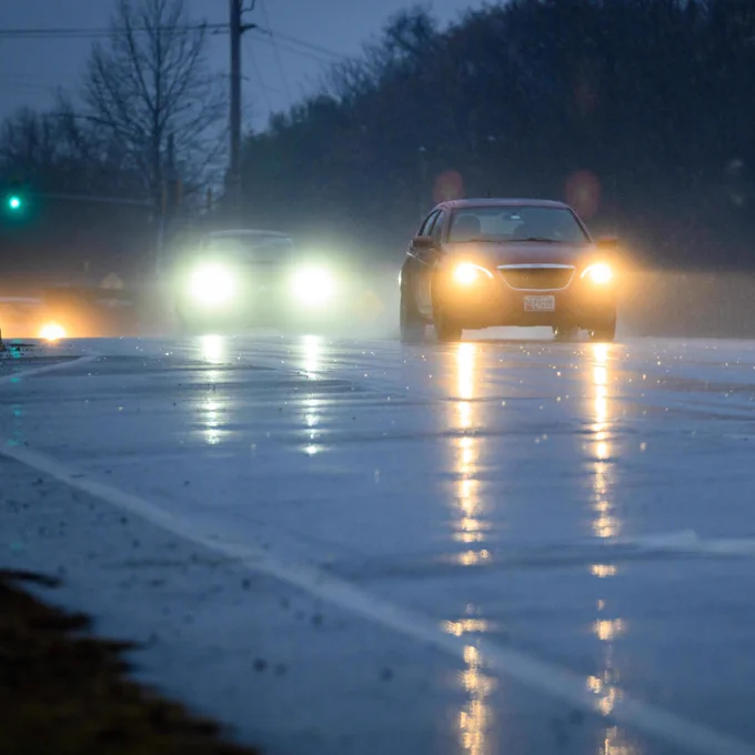 A car driving on a wet road with headlights reflecting on the pavement.
