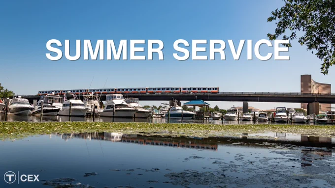 An Orange Line train crossing a bridge over the Mystic River with boats in a marina below.