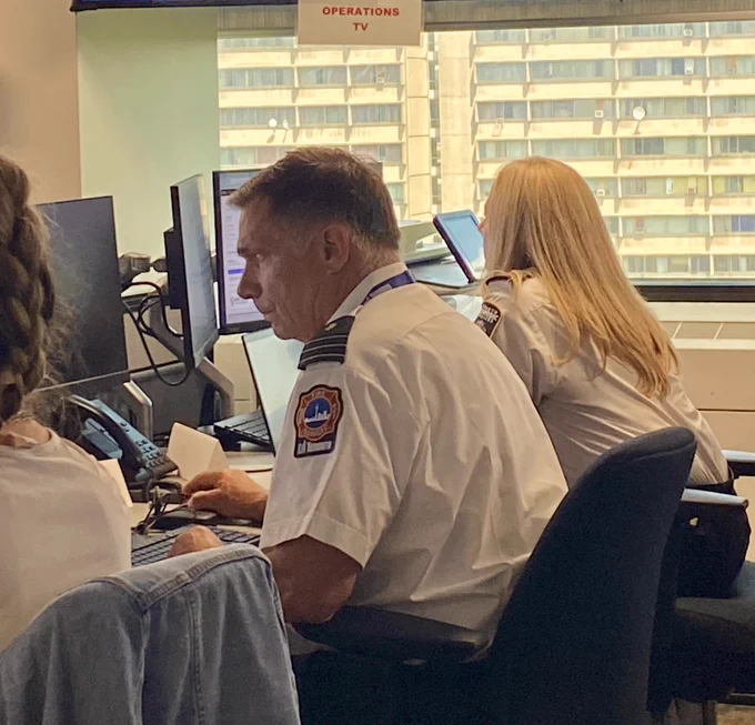 Toronto Fire Services staff sitting at a desk with a computer screen working. Beside him is a Paramedic staff member doing same.