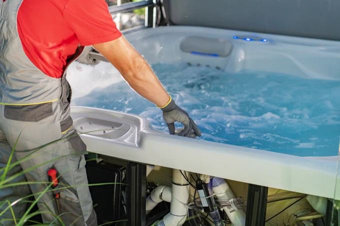 A technician, wearing overalls and gloves, does maintenance on hot tub.