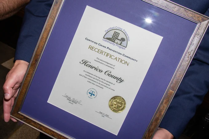Certificate of Recertification awarded to Henrico County for maintaining Certified Crime Prevention Community status, framed and held by a person.