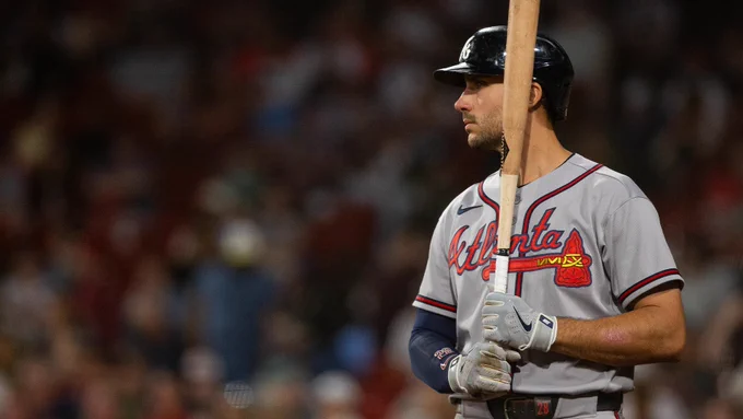 Baseball player Matt Olson of the Atlanta Braves. He stands holding a wooden baseball bat upright with both hands, looking forward with a calm, focused expression. He wears a gray Braves jersey with "Atlanta" displayed across the front, matching pants and a navy blue batting helmet. Behind him, the crowd in the stadium is out of focus.