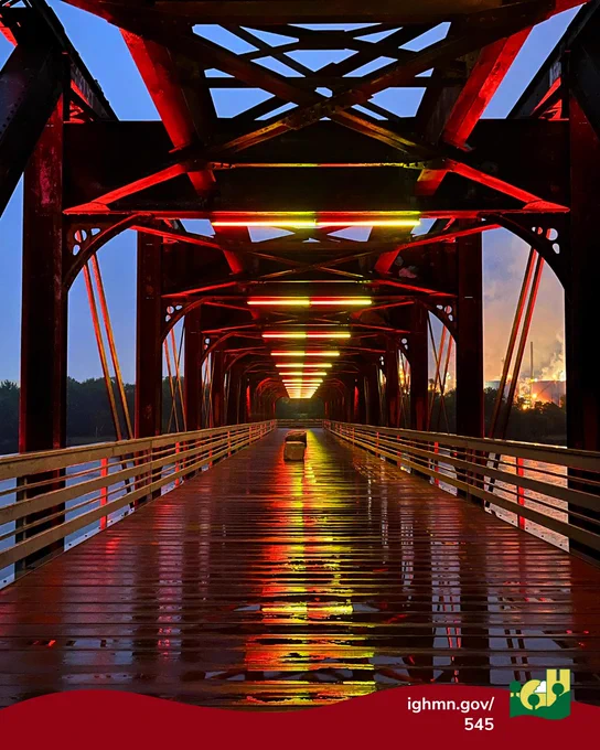 Illuminated Rock Island Swing Bridge at night with glowing yellow lights reflecting on wet wooden floorboards.