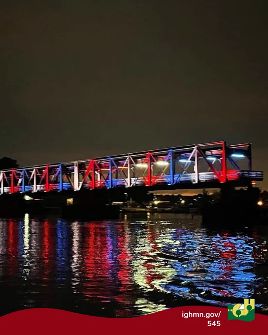 Rock Island Swing Bridge illuminated with red, white, and blue lights reflecting vividly on the calm river below at night.