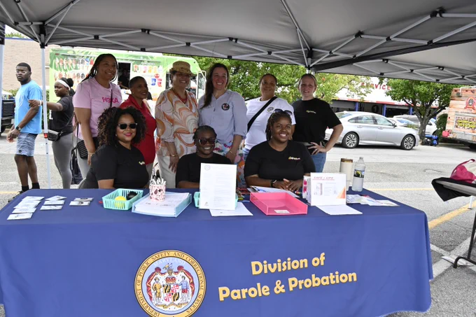 Group of people standing and sitting behind a Division of Parole & Probation table under a canopy at an outdoor event.