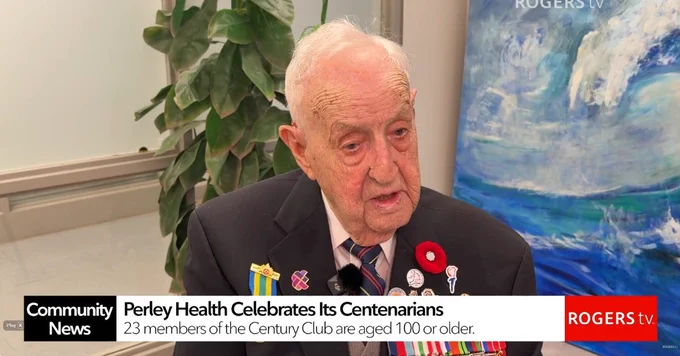 Veteran wearing medals and a poppy pin, seated indoors with a plant and a Rogers TV backdrop behind him.