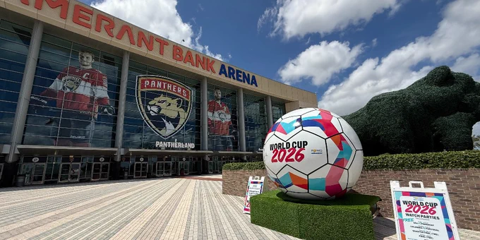 Giant colorful World Cup soccer ball outside an arena titled: Amerant Bank Arena. The ball is on a grassy platform sitting on a brick plaza.
