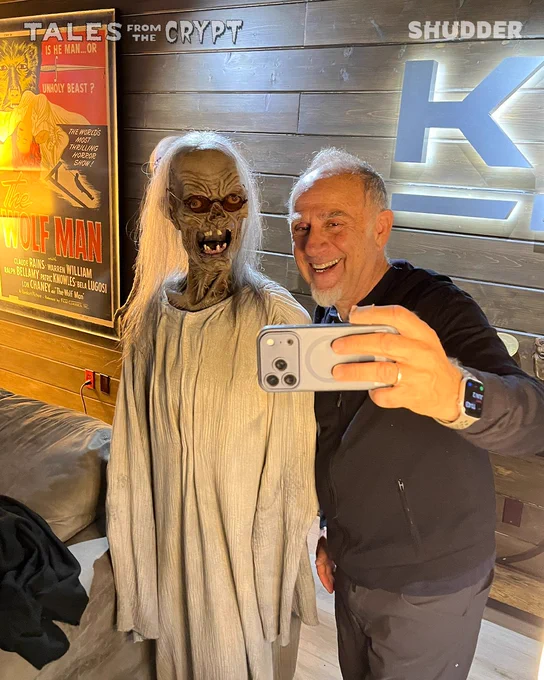 A man takes a selfie with a horror-themed figure in a spooky setting. The mood is playful and lighthearted, contrasting with the eerie surroundings.