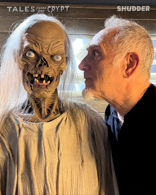 A man closely examines a 'Tales from the Crypt' creature. The scene mixes horror with curiosity.