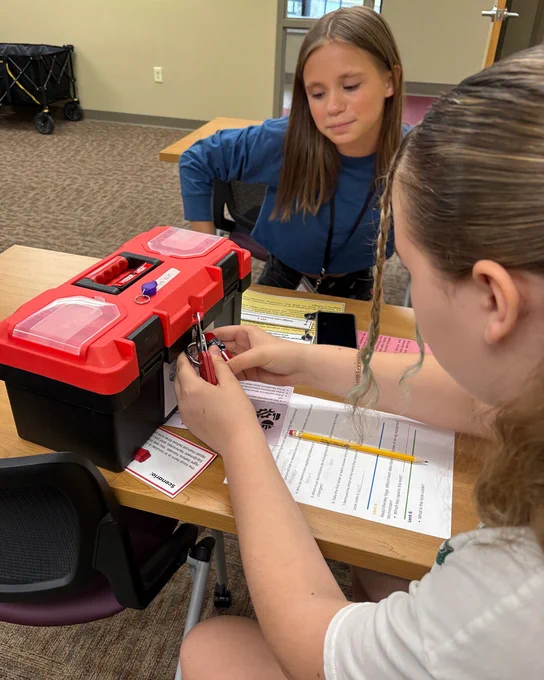 Two campers work together to unlock a red toolbox during a College Camp problem-solving activity.