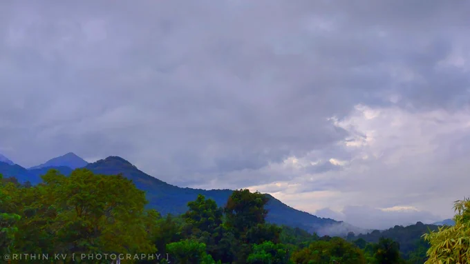 Lush green tropical mountains and misty hills under a heavy, overcast monsoon sky.