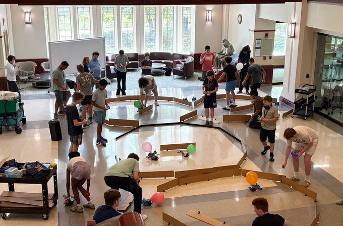 Notre Dame Engineering Innovation Hub Robotics Camp participants control robots in a friendly competition, maneuvering through barriers and trying to pop balloons attached to opposing robots.