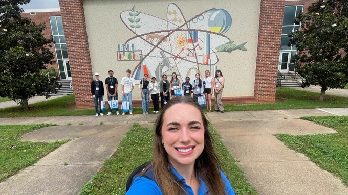 SOA takes selfie with students at orientation in the background in front of a science mural
