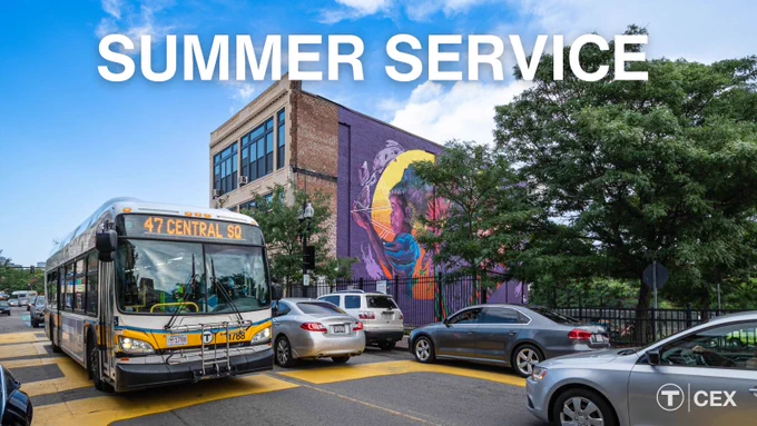 A MBTA Route 47 bus driving in Boston along parked cars on a summer day.
