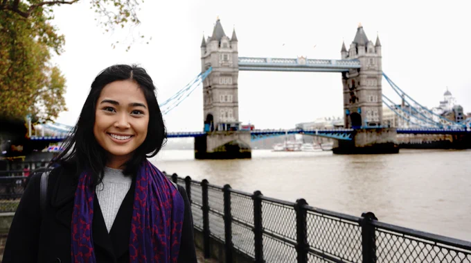 Person smiling by the Thames River with Tower Bridge in the background.