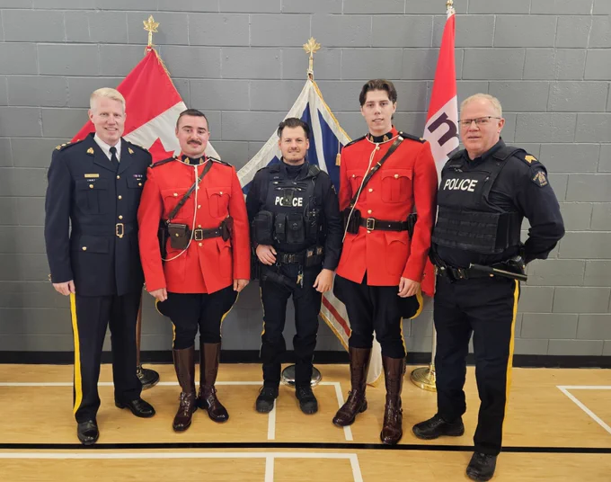 A group of RCMP officers stand together in front of flags at a ceremony for recognition of impaired driving arrests. 