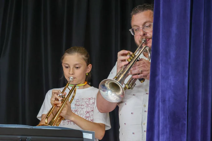 student and teacher play the trumpet together on stage