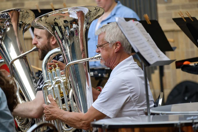 Musicians playing shiny silver tubas in an outdoor band performance by the Capital City Brass Band. 