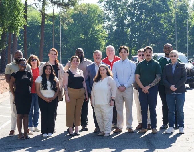 The Enterprise Security and Risk Management Office (ESRMO) team standing outdoors in a parking lot, posing for a group photo. There are trees and parked cars in the background, and everyone is dressed in business-casual attire.