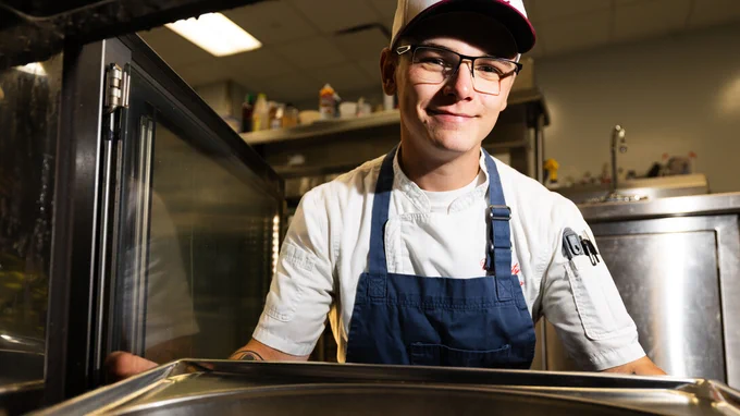 Drake Wiggins, catering production manager in University Dining Services, puts a tray in an oven in the catering kitchen. (Liz McCue/University Communication and Marketing)